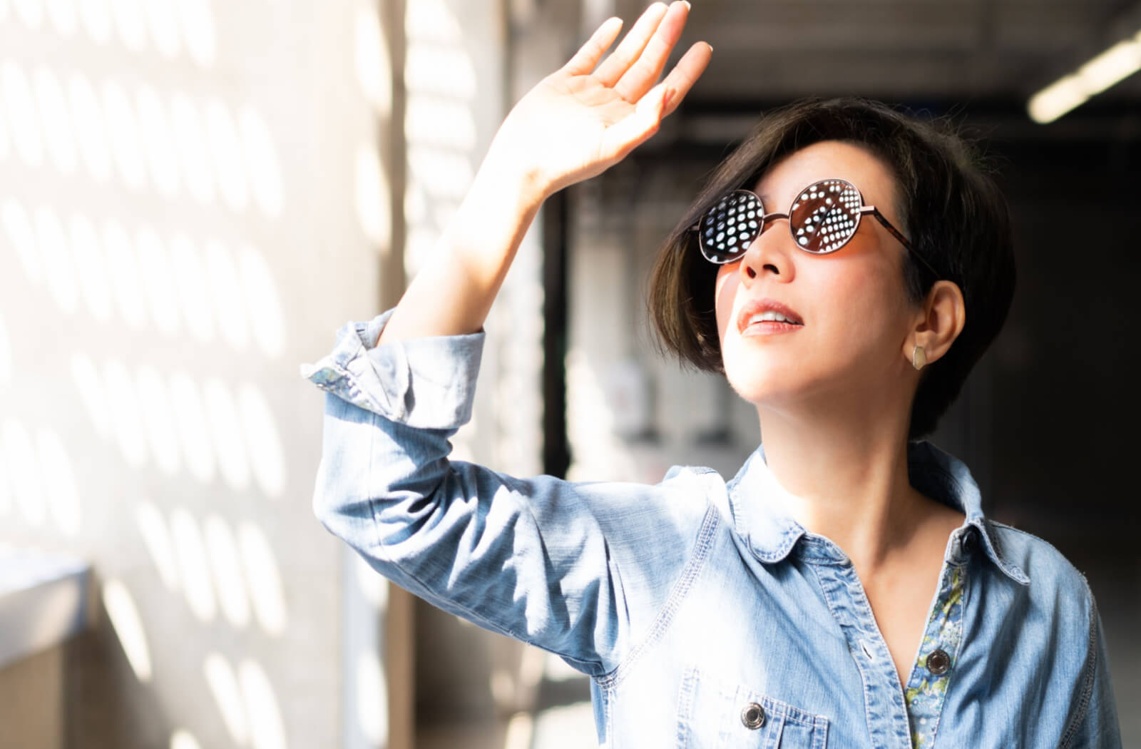 a woman wearing sunglasses holds her hand up to shield her eyes from the sun