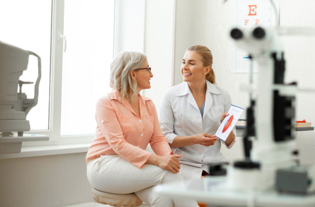 A female doctor is sitting beside her female patient while holding a paper material and showing it to her patient.